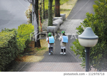 小學生放學的場景。雨後女孩撐著傘聊天開心走回家的後視圖 小學生放學的場景。雨後女孩撐著傘聊天開心走回家的後視圖 112978718