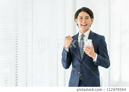 一位身穿西裝的年輕亞洲男性商人用智慧型手機擺姿勢 112979564