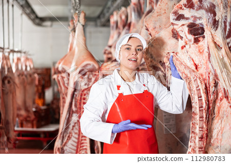 Female slaughterhouse worker showing beef chunk in meat storage 112980783