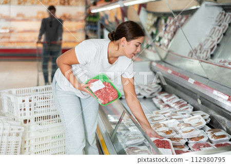 Attentive woman buying minced meat in the meat department of supermarket 112980795