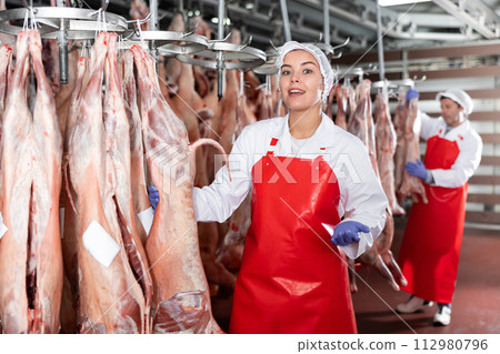 Female slaughterhouse worker showing mutton carcass in meat storage 112980796