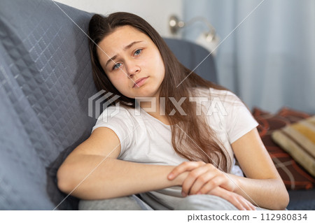 Depressed young woman sitting on sofa at home 112980834