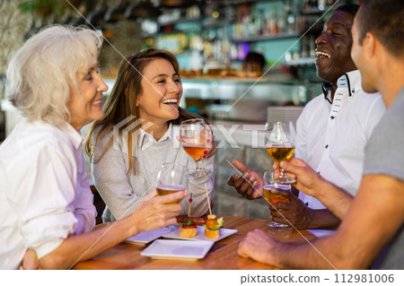 Funny females and males with drinks celebrating together at pub. Focus on young woman 112981006