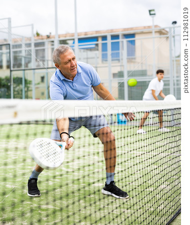 Unusual angle through tennis net on an elderly male padel player Unusual angle through tennis net on an elderly male padel player 112981019
