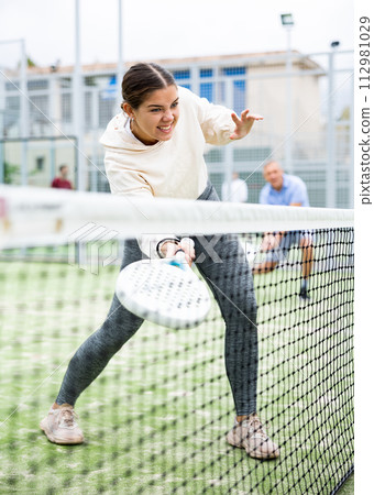 Woman serving ball while playing padel in court during training 112981029