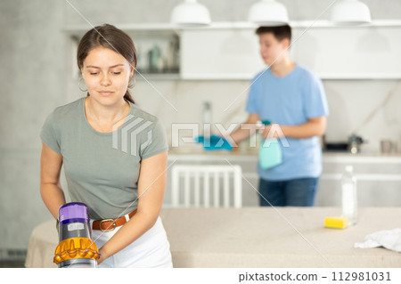 Young girl vacuum-cleaning in the kitchen while her husband dusting chandelier Young girl vacuum-cleaning in the kitchen while her husband dusting chandelier 112981031