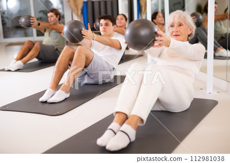 Sporty energetic males and females doing exercises with pilates ball during group training at gym. Fitness concept. Sporty energetic males and females doing exercises with pilates ball during group training at gym. Fitness concept. 112981038