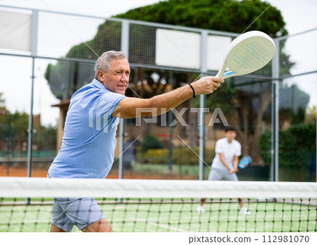 Aged man playing paddleball match on outdoor court Aged man playing paddleball match on outdoor court 112981070