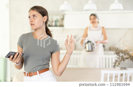 Young girl standing at the table while woman is quarreling with her standing behind 112981094