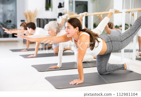 Positive young female performing set of exercises on a pilates mat during group class in fitness studio. 112981104