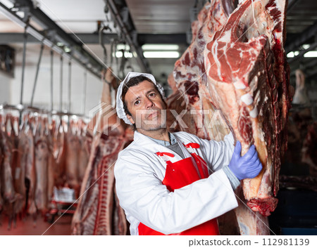 Male slaughterhouse worker showing beef chunk in meat storage 112981139