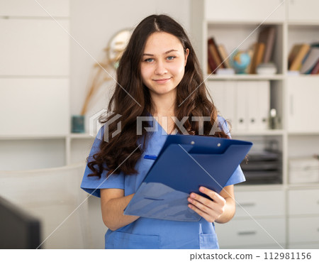 Doctor trainee who is undergoing an internship at the clinic makes important notes on a tablet while standing in a office Doctor trainee who is undergoing an internship at the clinic makes important notes on a tablet while standing in a office 112981156
