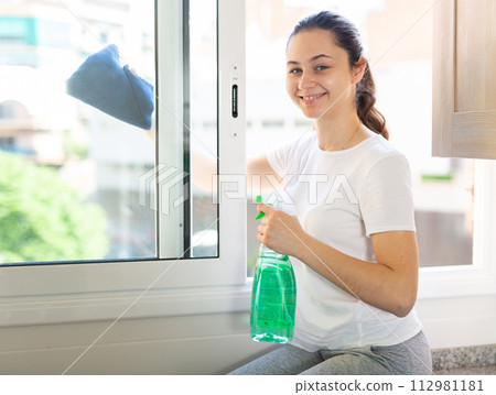Young housewife is cleaning window with detergent at home Young housewife is cleaning window with detergent at home 112981181