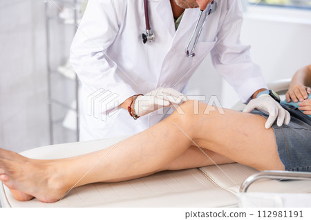 Attentive doctor man examining the sore knee of female patient 112981191
