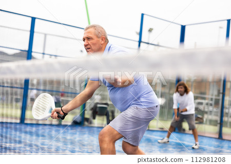 Portrait of serious mature male in sportswear enjoying popular sport padel game on tennis court outside Portrait of serious mature male in sportswear enjoying popular sport padel game on tennis court outside 112981208