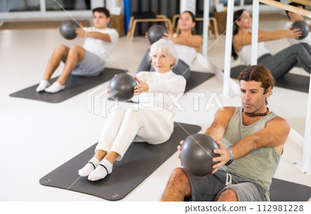 Men and women doing pilates exercises with fitness ball at gym 112981228