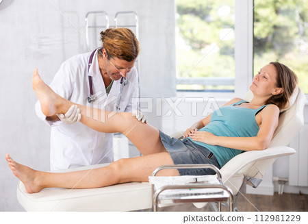 Professional orthopedic traumatologist examining leg and knee of young woman 112981229