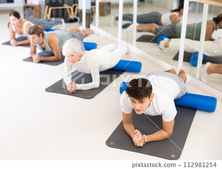 Young man practicing pilates with blue roller in gym room 112981254
