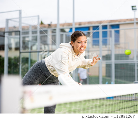 European young woman tennis player playing padel during friendly match on outdoor court in spring European young woman tennis player playing padel during friendly match on outdoor court in spring 112981267