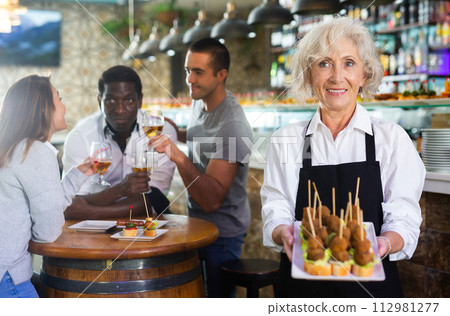 Mature female waiter holding tray with pinchos at restaurant Mature female waiter holding tray with pinchos at restaurant 112981277