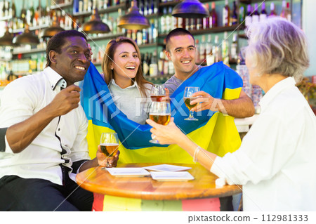 Excited male and female football fans celebrating championship win, waving flag of Ukraine in pub Excited male and female football fans celebrating championship win, waving flag of Ukraine in pub 112981333