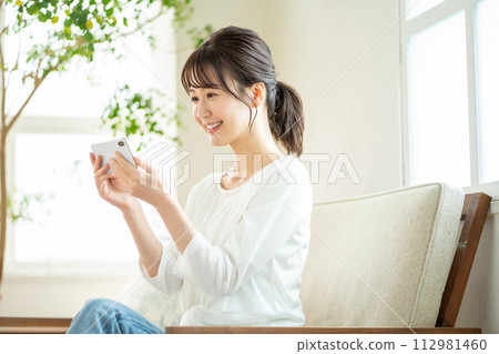 A woman who operates a smartphone, a smartphone at home A woman who operates a smartphone, a smartphone at home 112981460