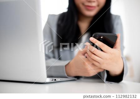 A cropped shot of an Asian businesswoman is using her smartphone at her desk in the office. A cropped shot of an Asian businesswoman is using her smartphone at her desk in the office. 112982132