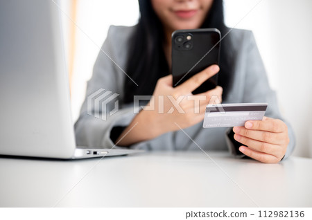 A businesswoman is holding a smartphone and a credit card, using online payment banking. A businesswoman is holding a smartphone and a credit card, using online payment banking. 112982136