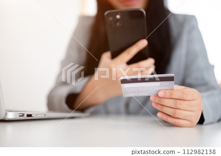 A businesswoman sitting at a table with her smartphone and a credit card, using a mobile banking app 112982138
