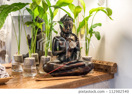 Spathiphyllum cochlearispathum commonly called peace lily growing in water in glass, with buddha Spathiphyllum cochlearispathum commonly called peace lily growing in water in glass, with buddha 112982540