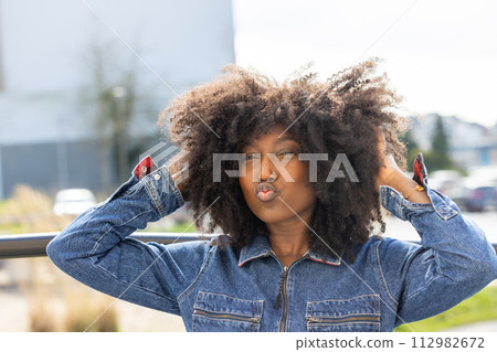 Joyful African American Woman in Denim Jacket Making a Kissy Face Outdoors Joyful African American Woman in Denim Jacket Making a Kissy Face Outdoors 112982672