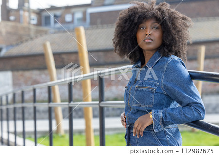 Stylish Woman in Denim with Afro Hair Posing in an Urban Landscape Stylish Woman in Denim with Afro Hair Posing in an Urban Landscape 112982675