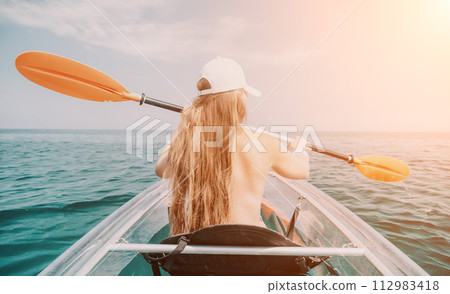 Woman in kayak back view. Happy young woman with long hair floating in transparent kayak on the crystal clear sea. Summer holiday vacation and cheerful female people relaxing having fun on the boat Woman in kayak back view. Happy young woman with long hair floating in transparent kayak on the crystal clear sea. Summer holiday vacation and cheerful female people relaxing having fun on the boat 112983418