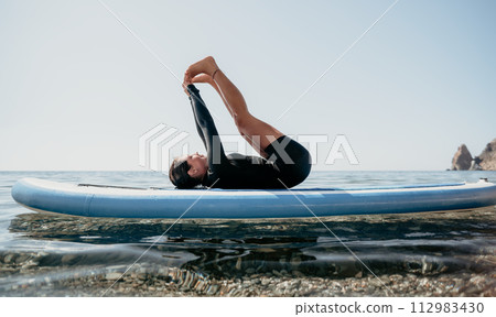 Woman sup yoga. Happy sporty woman practising yoga pilates on paddle sup surfboard. Female stretching doing workout on sea water. Modern individual female hipster outdoor summer sport activity. 112983430