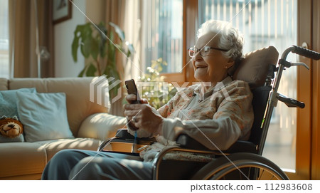 Elderly woman in a wheelchair at home using a smartphone, showcasing independence. Cozy interior, natural light. A moment of technology and age intersection. AI 112983608