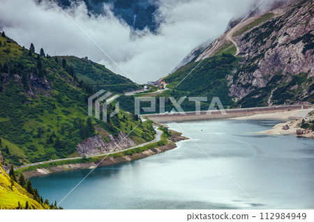 landscape with mountains, hills, Fedaia lake, trees and fog 112984949
