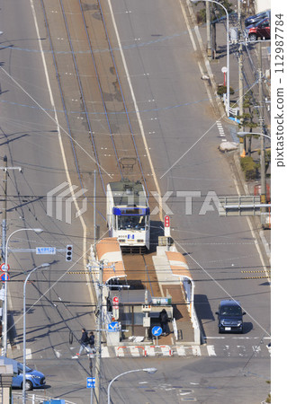 [Vertical composition/person number logo retouched] Hakodate City Tram entering Yachigashira stop and departing 112987784