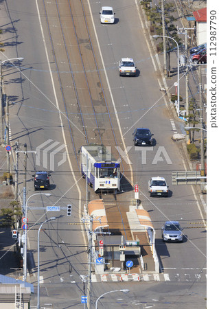 [Vertical composition/person number logo retouched] Hakodate City Tram entering Yachigashira stop and departing 112987790
