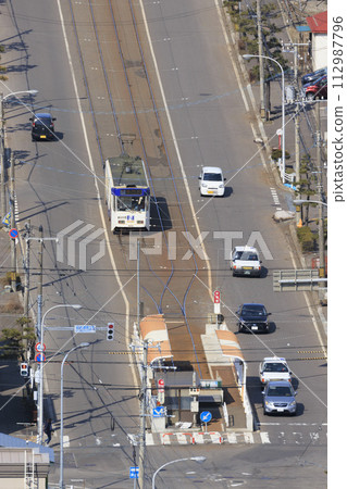 [Vertical composition/person number logo retouched] Hakodate City Tram entering Yachigashira stop and departing 112987796