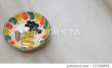 A small plate with various health supplement pills and capsules. On a marble surface, with copy space on the right. 112988898