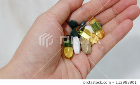 Closeup of hand holding assorted supplement pills and capsules.  112988901
