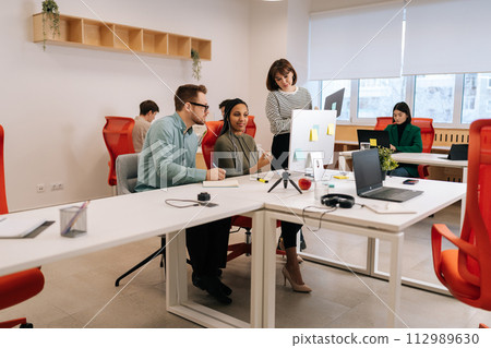 Remote view of diverse colleagues working together discussing computer project teamwork. Multiethnic business people of startup team coworkers cooperating sitting at work in modern corporate office. Remote view of diverse colleagues working together discussing computer project teamwork. Multiethnic business people of startup team coworkers cooperating sitting at work in modern corporate office. 112989630