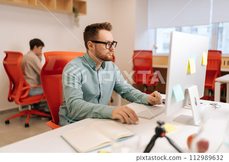 Modern corporate office open space with busy male and female staff employees using laptop computers sitting at work in big modern corporate office. Startup team working together at creative open space Modern corporate office open space with busy male and female staff employees using laptop computers sitting at work in big modern corporate office. Startup team working together at creative open space 112989632