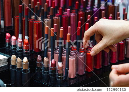 Woman chooses a lipstick in a cosmetics store. Woman chooses a lipstick in a cosmetics store. 112990180