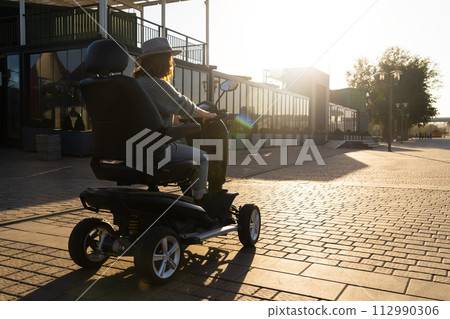 Woman tourist riding a four wheel mobility electric scooter on a city street Woman tourist riding a four wheel mobility electric scooter on a city street 112990306