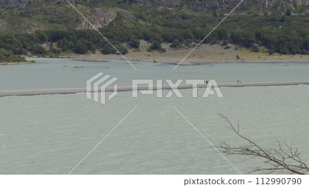 Hikers on a Narrow Sand Strip Between Glacial Waters 112990790