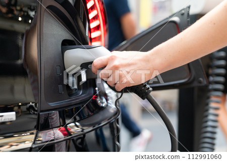 Woman holding plug of electric car charging station Woman holding plug of electric car charging station 112991060