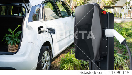 Charging electric car in the yard of a country house Charging electric car in the yard of a country house 112991349
