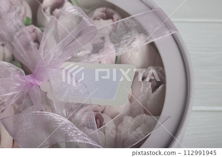 Zephyr in a box. Marshmallow tulips. The box is pink, tied with a ribbon. View from above. Close-up. On a white background. 112991945