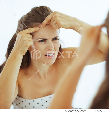 Concerned young woman squeezing acne in bathroom Concerned young woman squeezing acne in bathroom 112992788